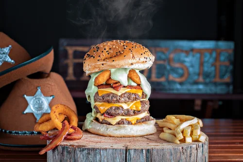 Hambúrguer triplo artesanal monstro com molho da casa verde escorrendo, onion rings e bacon